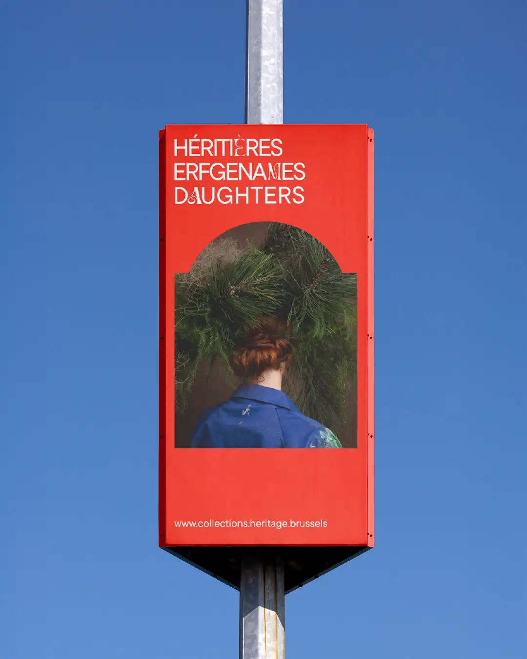 Héritières street furniture installation red: trilingual title, photo Barbara Salomé Felgenhauer artist back with giant floral arrangement head blue apron, collectionsheritiere.brussels, urban lamppost azure sky