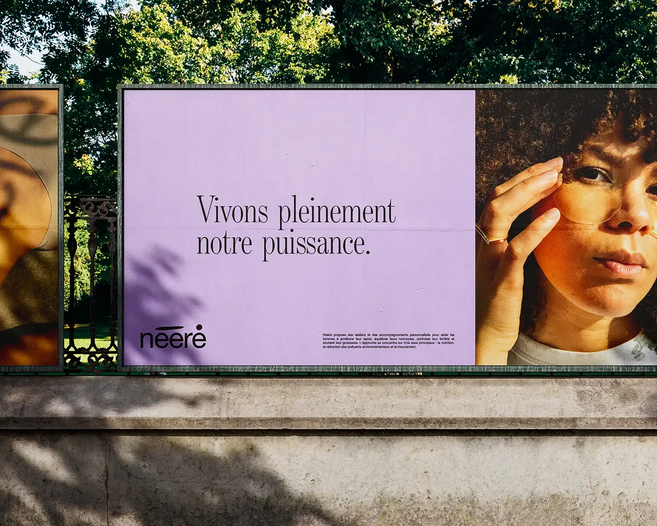Panneau publicitaire à l’entrée d’un parc urbain affichant la campagne de branding de la marque Nééré, incluant son logo et le slogan « Vivons pleinement notre puissance », conception visuelle signée Studio La Folie.