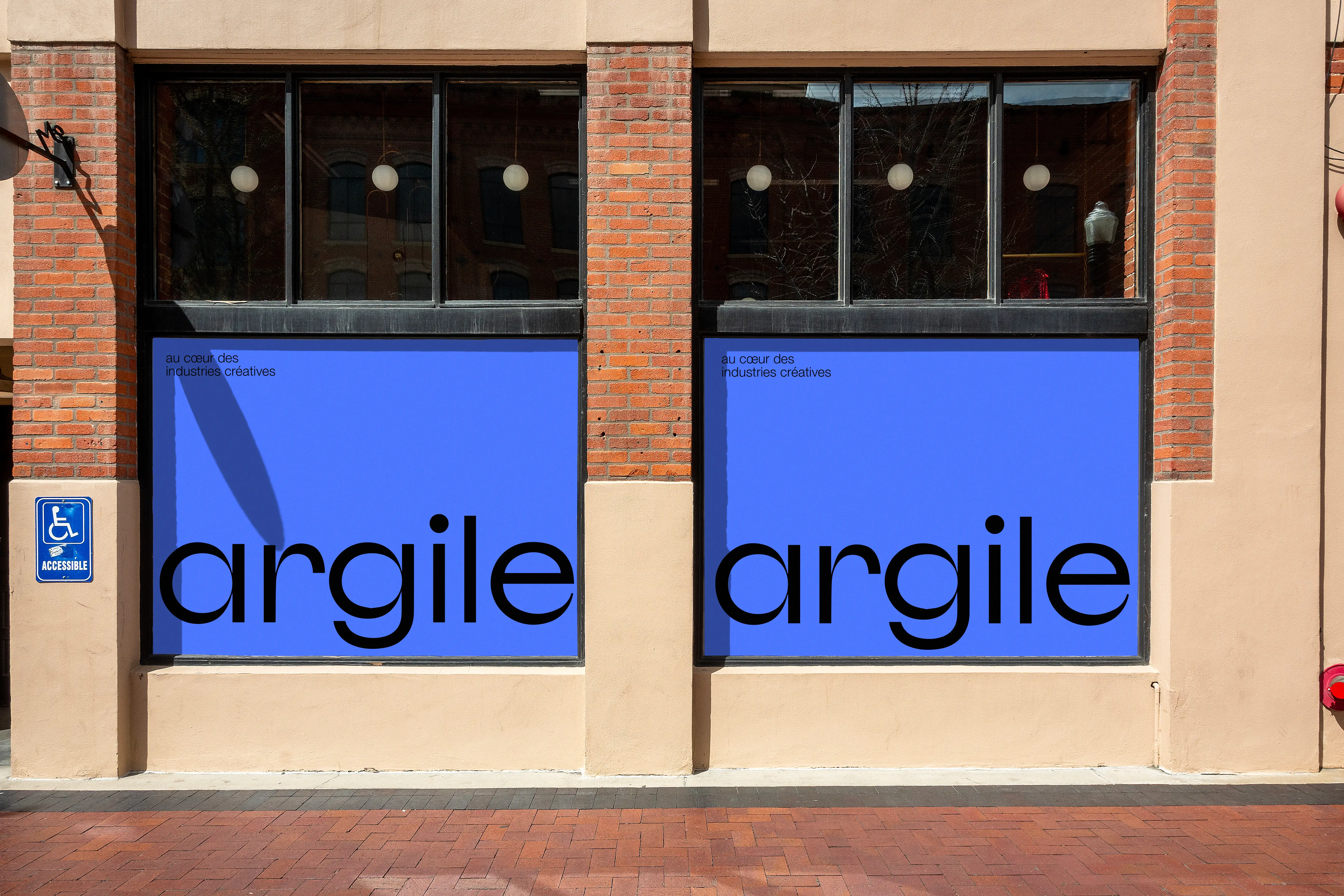 Bold blue Argile window decals on two windows of Brooklyn-style brick building, tagline "At the heart of creative industries" upper left corner