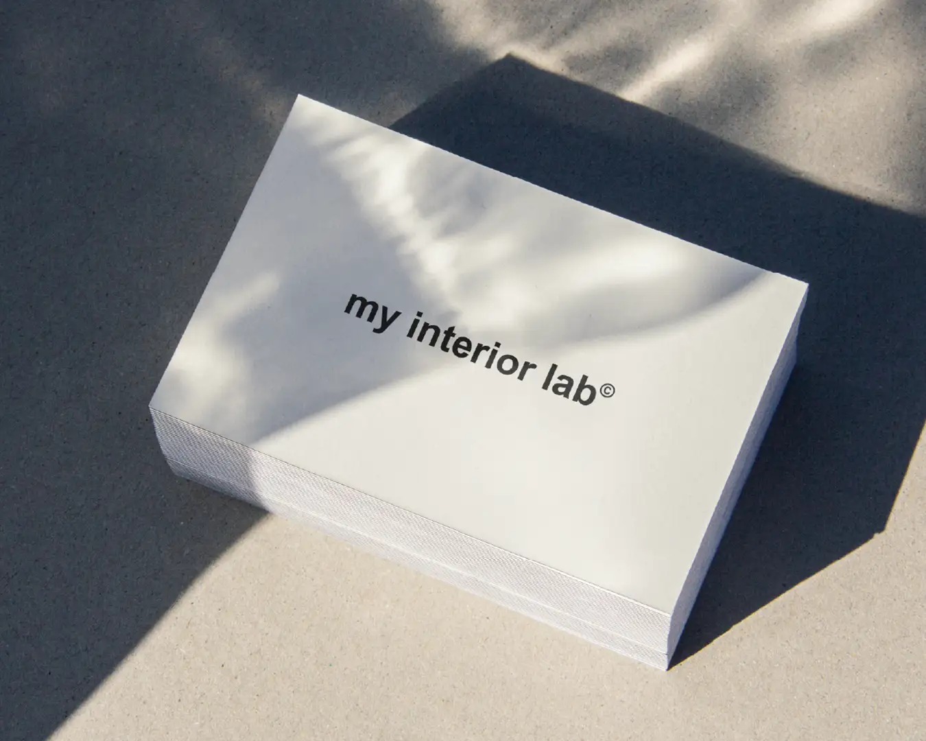 Gros plan sur un tas de cartes de visite pour le bureau d’architecture d’intérieur et mobilier MY INTERIOR LAB, texte noir sur fond clair, posées sur un sol brut type béton lissé, style minimaliste, design réalisé par Studio La Folie.