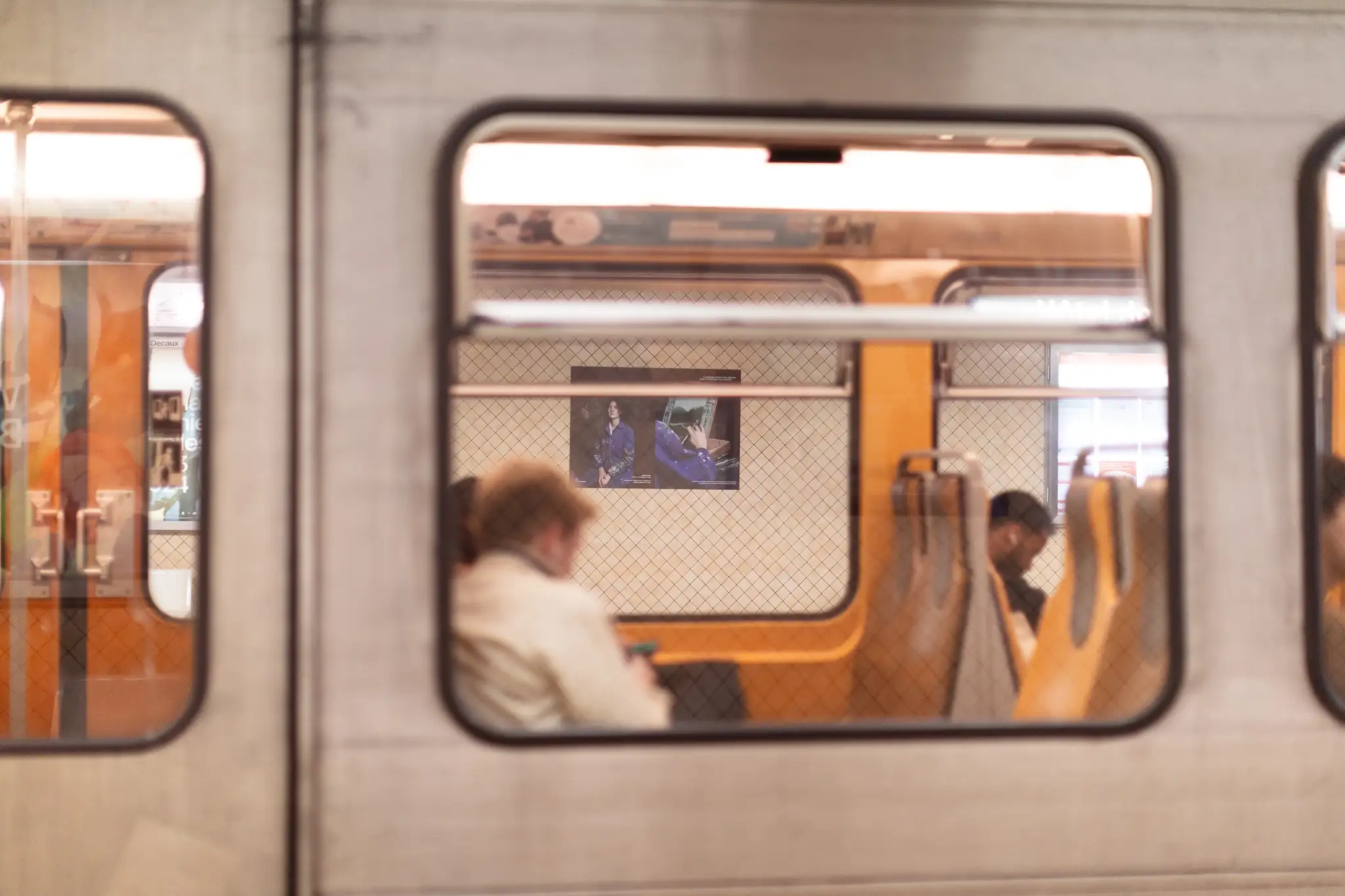 Photo by Barbara Salomé Felgenhauer at Brussels Monnaie metro station: commuters in foreground, platform view through window showing Héritières 2023 exhibition poster with Urban Brussels, authentic urban scene