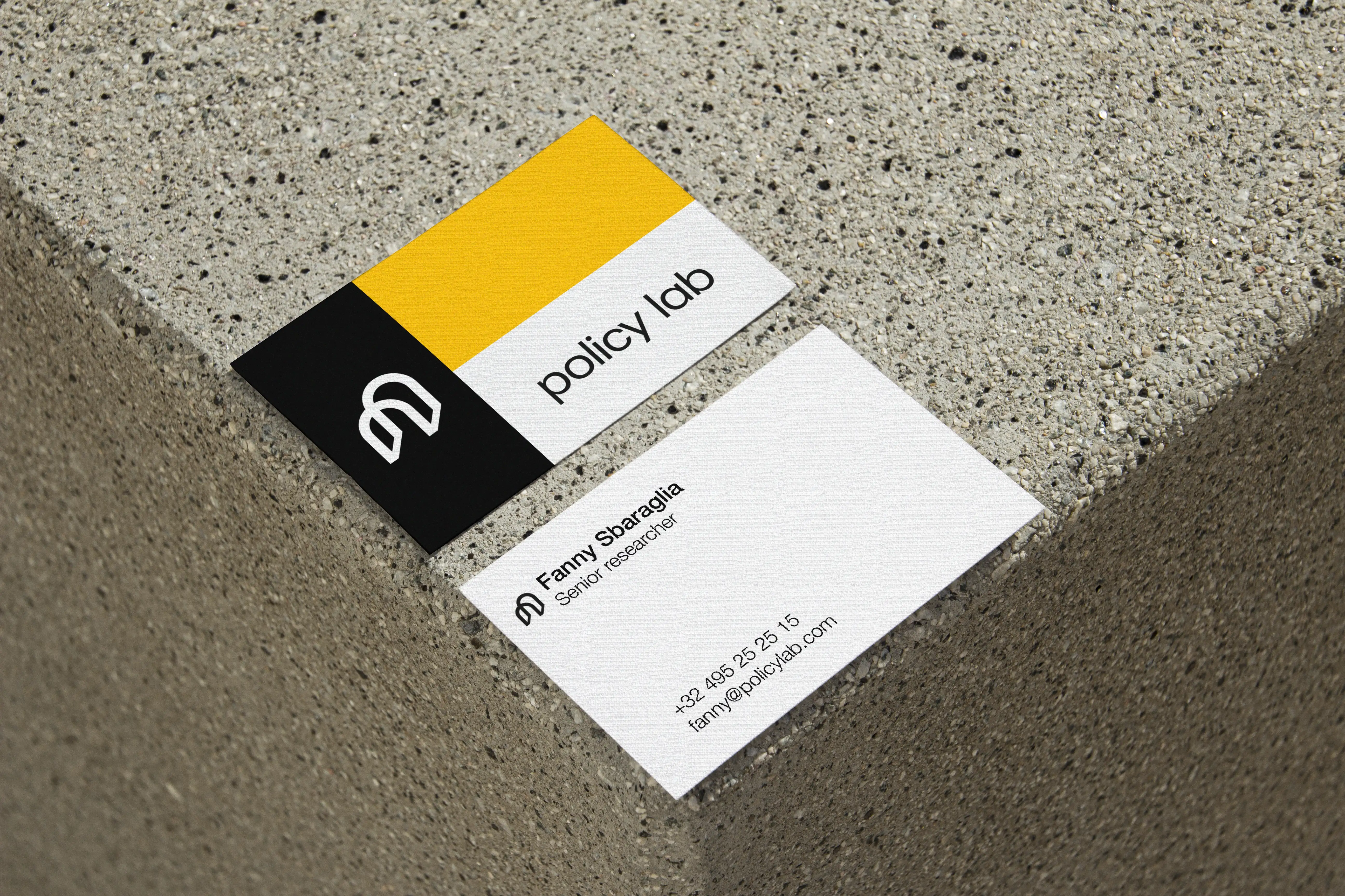 Policy Lab business card front and back placed on concrete cinder block edge, employee contact details with logo, minimalist industrial raw design
