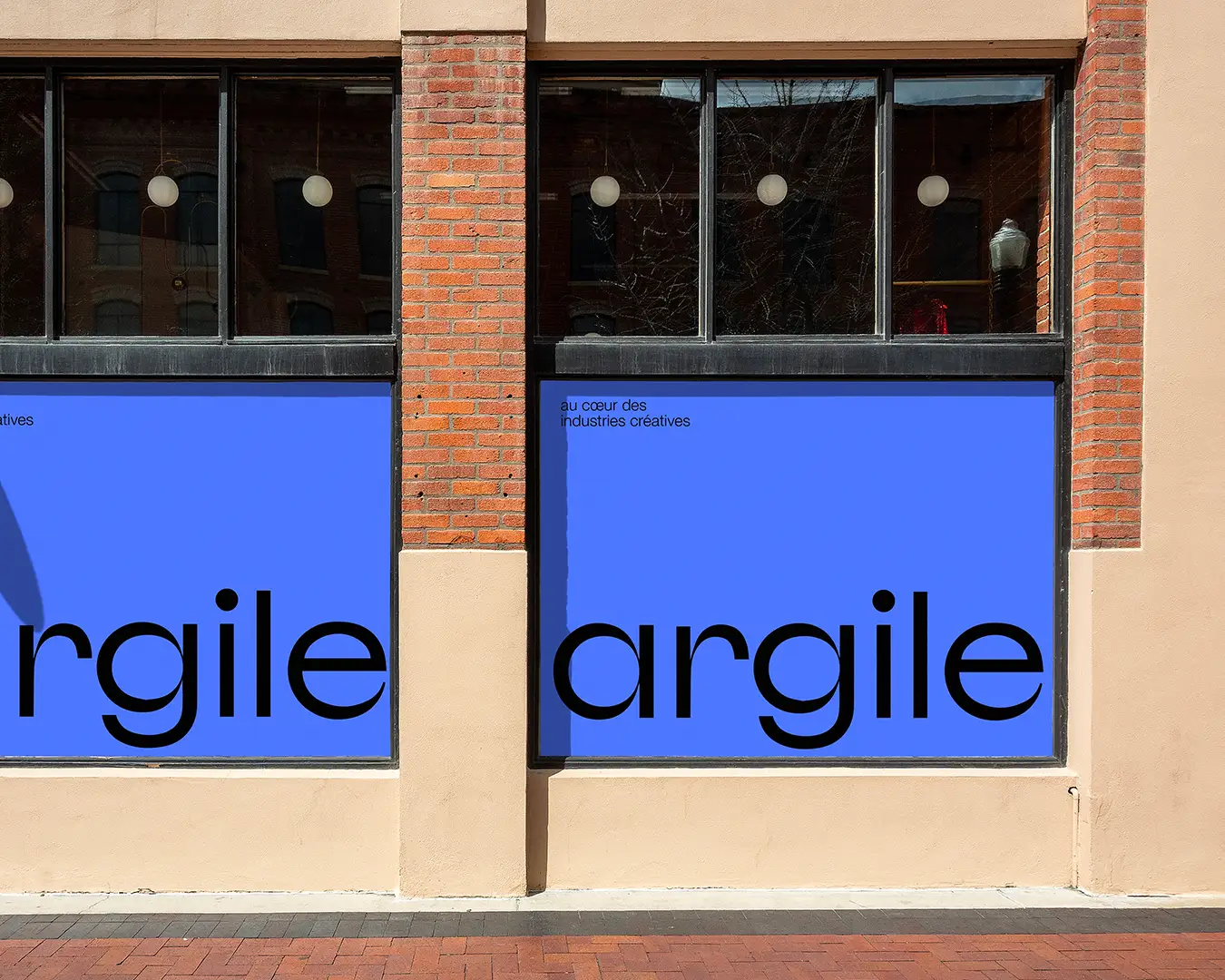 Façade de bureau citadin type Brooklyn pour ARGILE, bâtiment en pierres rouges, deux grandes fenêtres recouvertes d’une vitrophanie complète bleu lavande minimaliste, logo noir en grand, design et identité visuelle par Studio La Folie.