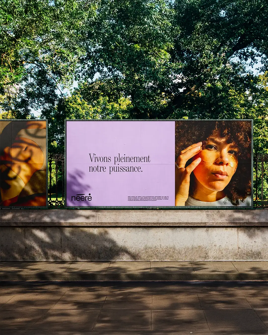 Dual-sided Nééré billboard in park setting: "Live our power fully" baseline on lilac with logo left panel, founder Véronique portrait closeup right