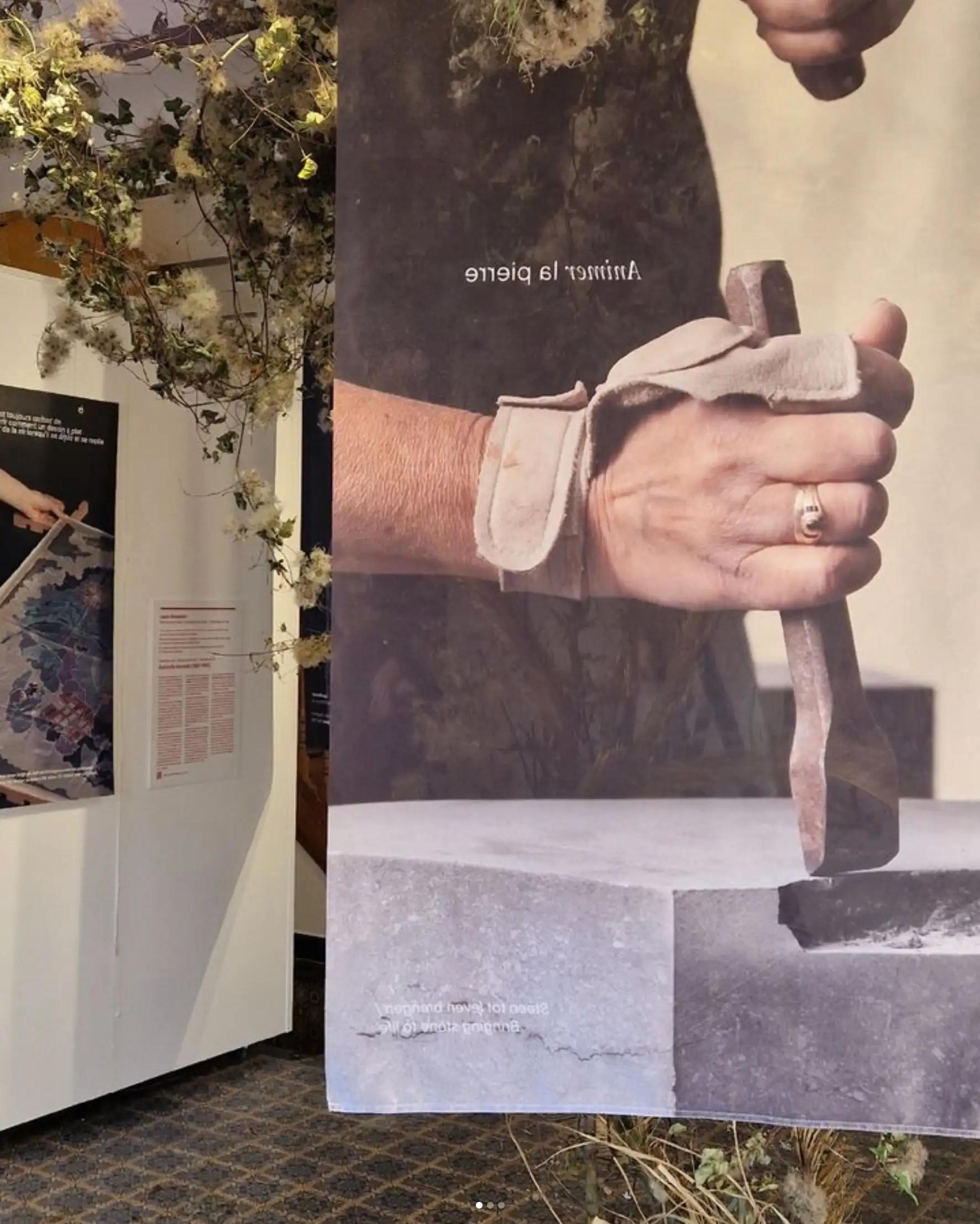 Close-up Héritières exhibition photo printed on suspended fabric banner: female sculptor with tool and stone, floral composition visible, aerial textile museum display