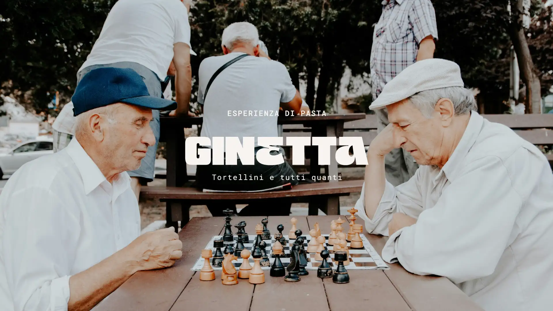 Authentic scene of two nonos playing chess, moment of Italian transmission and conviviality, "Esperienza di Pasta" text and Ginetta logo in white, Studio La Folie brand identity
